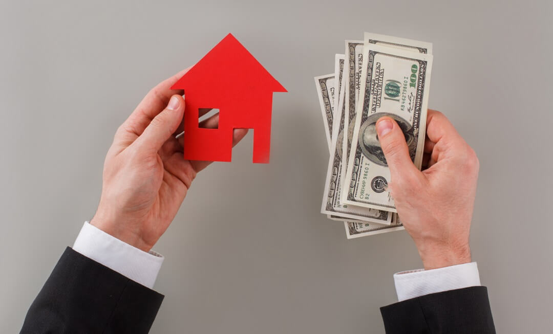 Male hands holding dollar banknotes and red paper house.