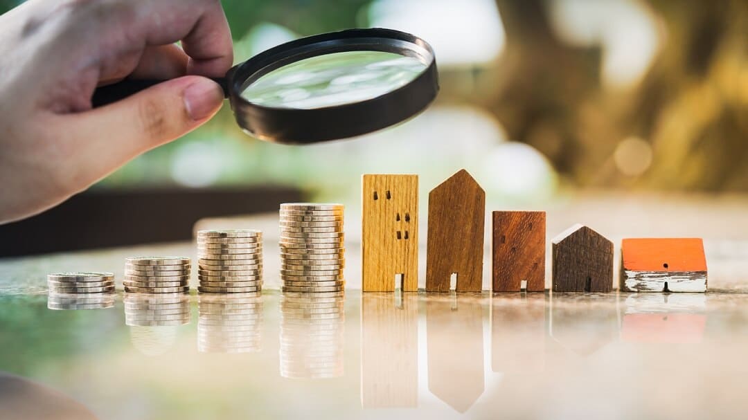 Hand holding magnifying glass and looking at house model with row of coin money