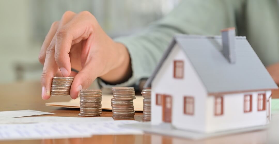 Man putting stack of coins on table with a model house.