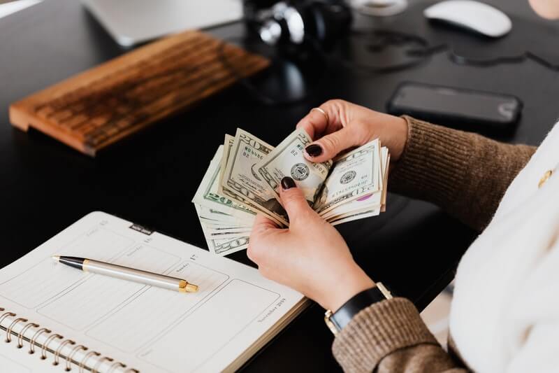 Man counting stack of money on a desk with notebook and pen