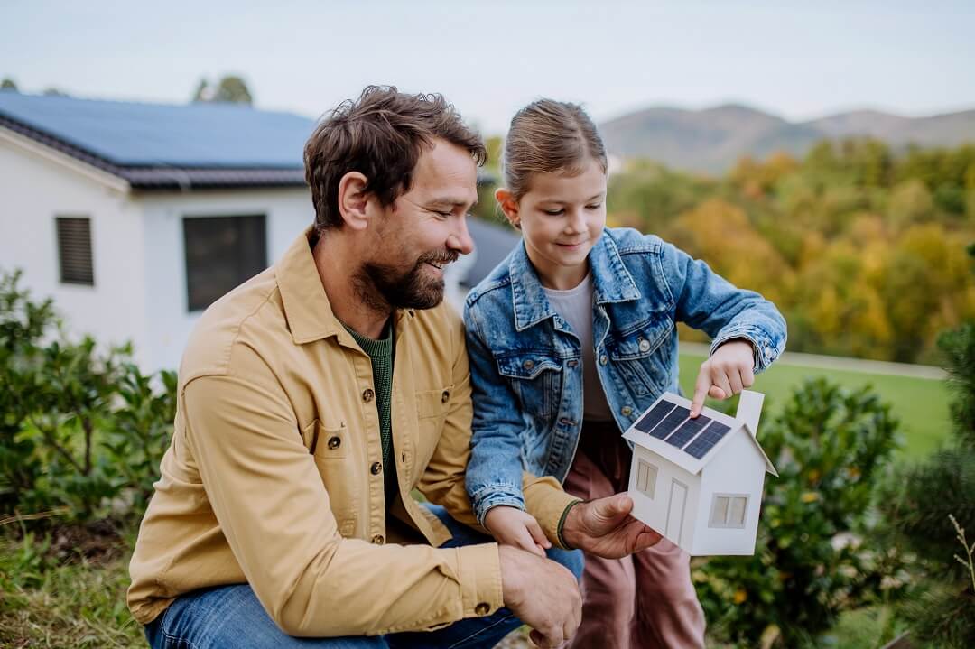 Little girl with her dad holding paper model of house with solar panels